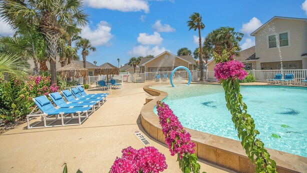 Uma área de piscina com espreguiçadeiras, piscina e uma casa ao fundo.
