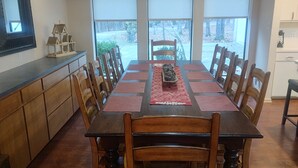 A dining room with a long wooden table, surrounded by wooden chairs, and a kitchen area with a wooden cabinet and a countertop.