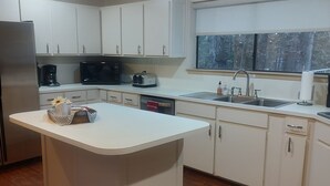A modern kitchen with white cabinets, a central island, and a window with a view of trees.
