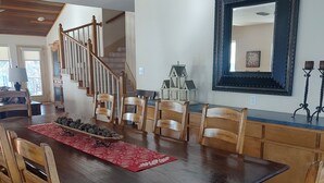 A dining area with a large wooden table, wooden chairs, a red placemat, and a decorative pine cone arrangement.