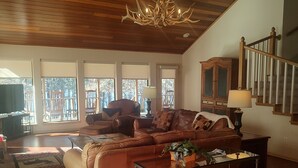 A spacious living room with a high ceiling, a large window, and a staircase.
