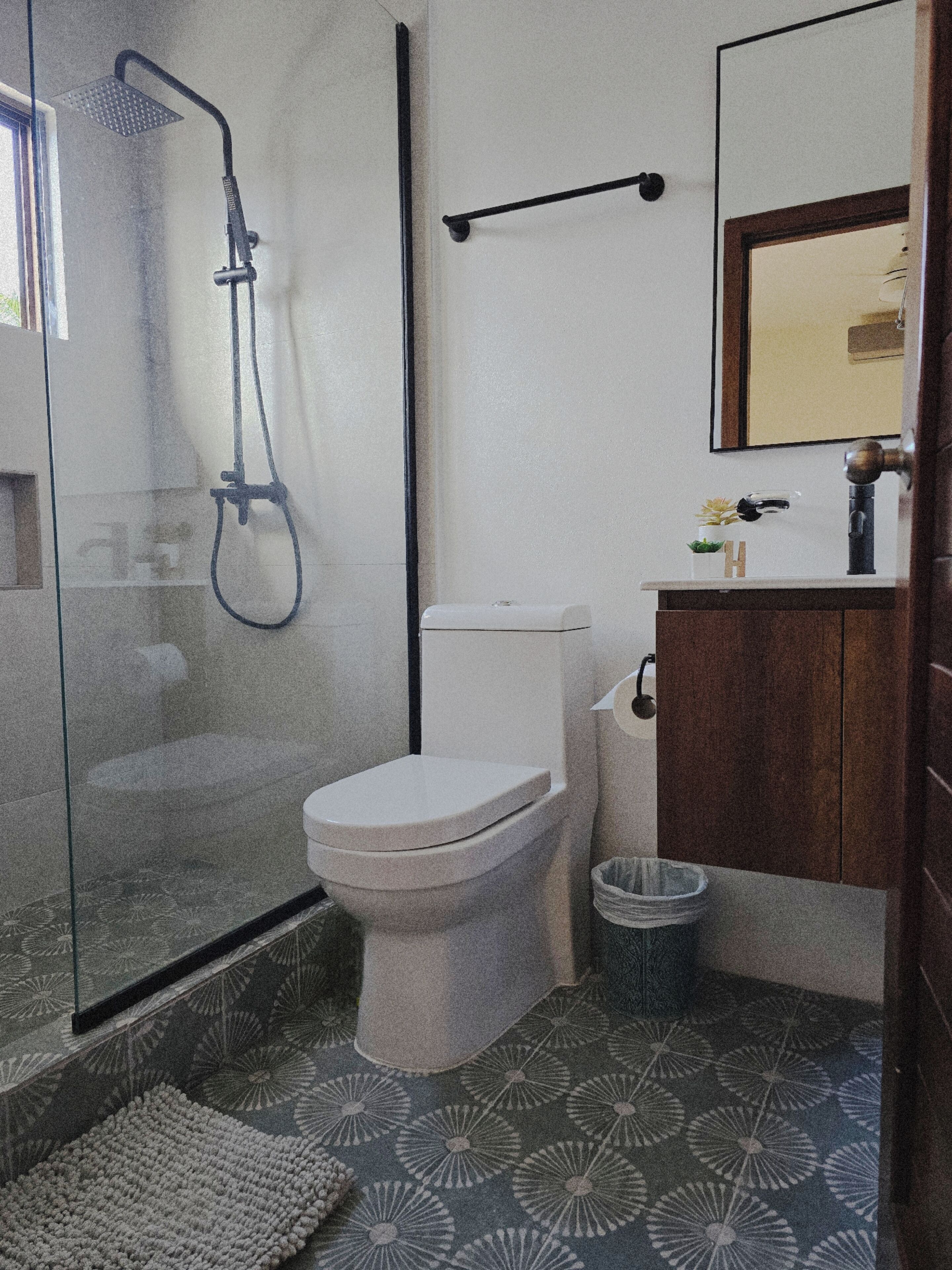 A modern bathroom with a glass-enclosed shower, a white toilet, and a wooden vanity with a mirror.