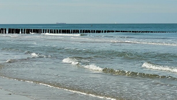 Une plage avec des vagues et une jetée en bois.
