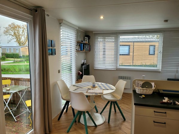 A dining area with a round table and four chairs, a kitchen area with a counter and cabinets, and a view of a house through the window.