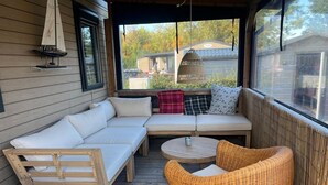 Un espace extérieur aménagé, abrité, avec un canapé, une petite table et des chaises en osier.