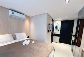 A modern hotel room with a bed, a wall-mounted air conditioner, a bathroom with a mirror, and a door leading to another room. - Alta Marine - Miramar Hospedagens  (João Pessoa)