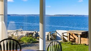 A seaside view from a room with a large window, a wooden table, and chairs. - The Harrington Hideaway (Coupeville)