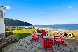 A patio with red Adirondack chairs, a small table, and a view of the ocean. - The Harrington Hideaway (Coupeville)