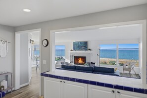 A modern kitchen with a fireplace, a dining area with a view of the ocean, and a living room with a sofa and a chair. - The Harrington Hideaway (Coupeville)