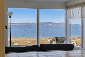 A room with a large window overlooking a wooden dock and the sea. - The Harrington Hideaway (Coupeville)