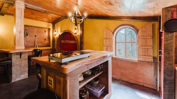 A rustic kitchen with wooden beams, a central island with a stove, and a window with wooden shutters. - Hobbit House in Cliffview Resort, Artisan Crafted, Themed. Centrally Located (Campton)