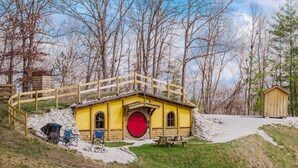 A yellow building with a red door, a wooden bridge, and a picnic table. - Hobbit House in Cliffview Resort, Artisan Crafted, Themed. Centrally Located (Campton)