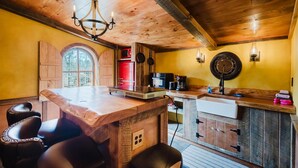 A kitchen with wooden cabinets, a central island, bar stools, a chandelier, and a large window. - Hobbit House in Cliffview Resort, Artisan Crafted, Themed. Centrally Located (Campton)