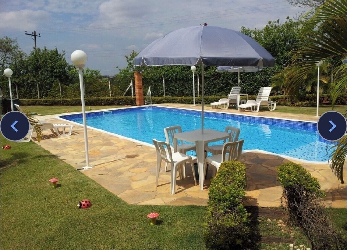Una piscina con una mesa y sillas, rodeada por un césped cuidado y un gran paraguas.