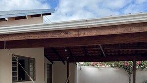 A covered patio area with a hammock, a concrete floor, and a white wall with a window. - Village house in Ponte Alta Babilônia - Serra da Canastra MG (Babilônia)