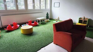 A room with a red sofa, green artificial grass, a small table, and a window with a view of trees. - Escapade alpine pour 6 en plein nature | BBQ (Lélex)
