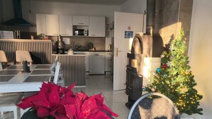 Une cuisine moderne avec des meubles blancs, un four à micro-ondes et une machine à café. On y trouve un coin repas avec une table et des chaises, ainsi qu’un sapin de Noël décoré de guirlandes lumineuses et d’ornements.