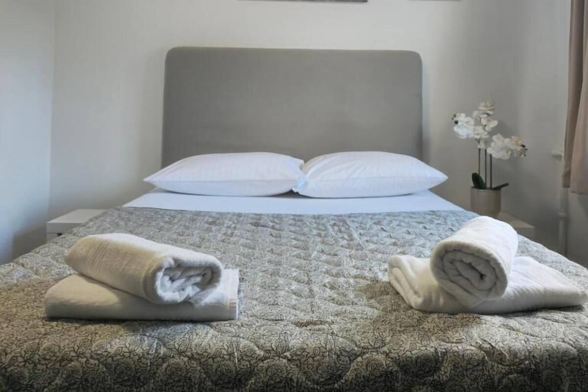 Un lit bien fait, recouvert d’une couvre-lit à motifs, avec deux oreillers et des serviettes enroulées posées sur le côté. Trois œuvres d’art encadrées sont accrochées au mur, au-dessus du lit.