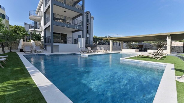 Un edificio moderno de dos pisos con piscina, mobiliario exterior y una pared de piedra.