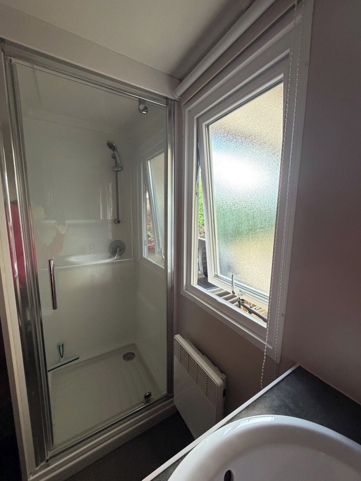 Ein Badezimmer mit Duschkabine, Fenster und weißem Waschbecken.