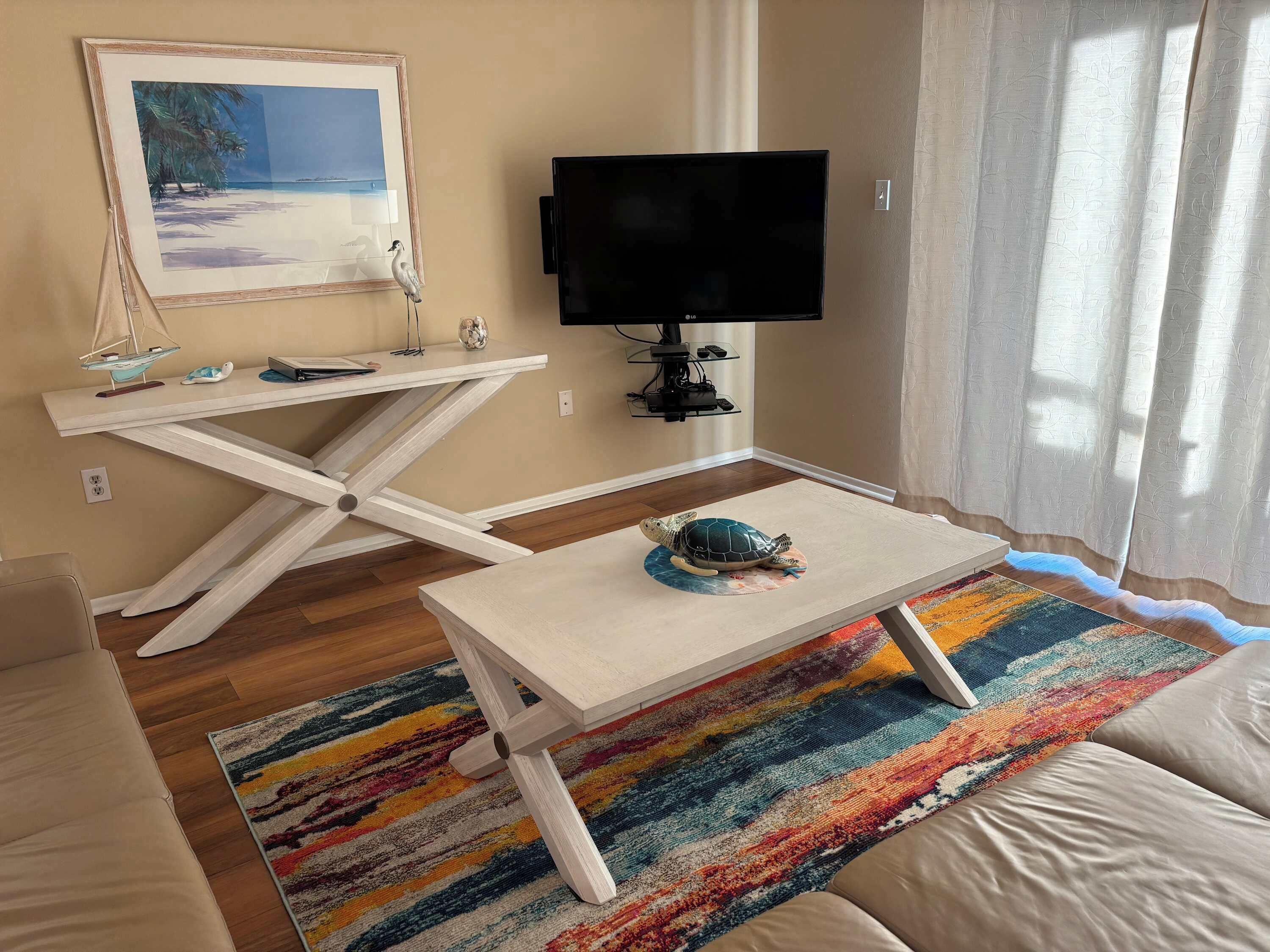 A living room with a TV, a painting, a table with a turtle figurine, and a colorful rug.