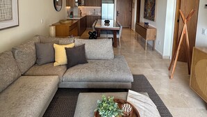 Un salon moderne avec un canapé d’angle gris, une table basse en bois agrémentée d’objets décoratifs et un ventilateur de plafond.