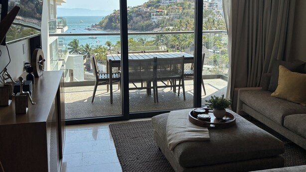 Un salon moderne doté d’une grande porte-fenêtre coulissante donnant sur un balcon avec vue sur la côte.