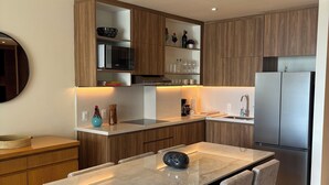 Une cuisine moderne avec des meubles en bois, un réfrigérateur en acier inoxydable et une table à manger en marbre, accompagnée de quatre chaises.