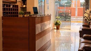 Et hotellets receptionsområde med en træreception, en bærbar computer, en potteplante og en lædersofa.