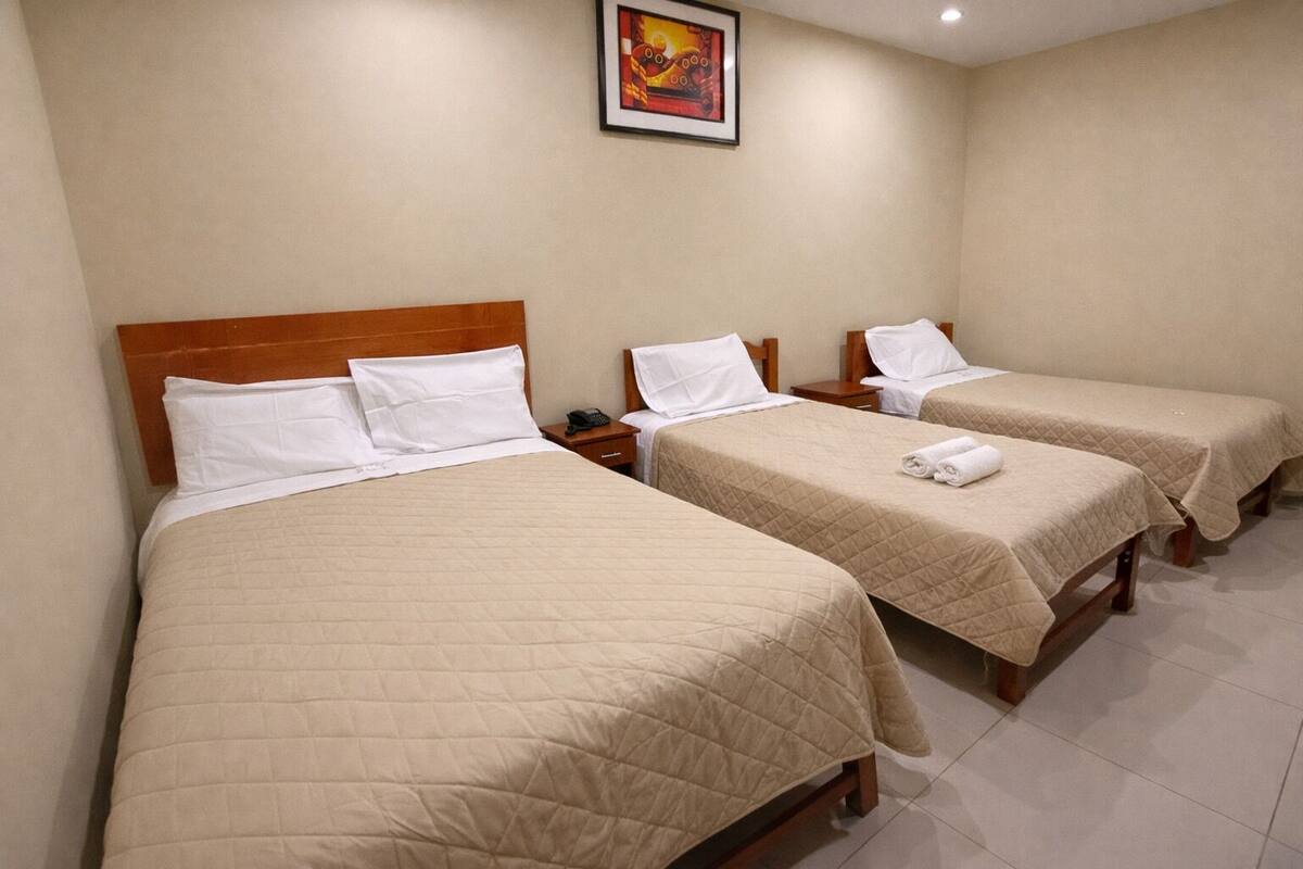 A hotel room with three single beds, each with a wooden headboard, white bedding, and a bedside table with a phone.