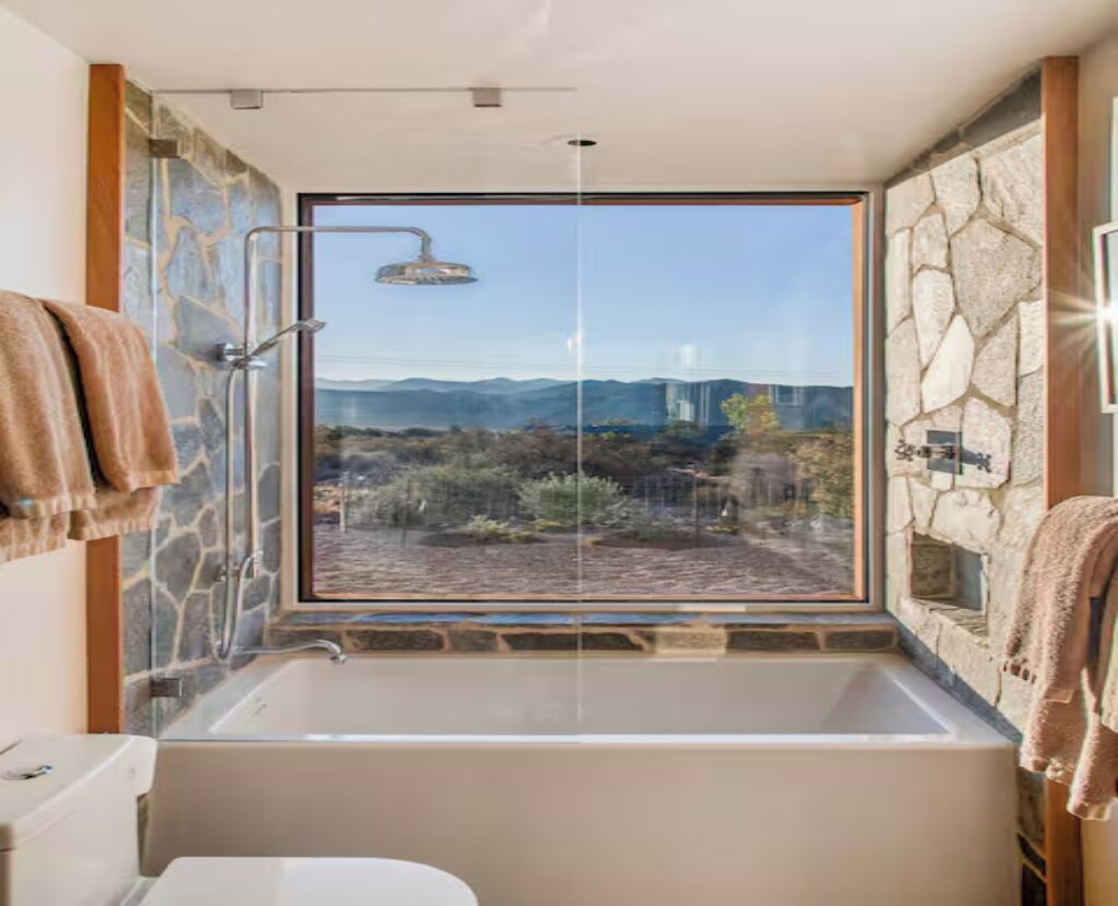 Un baño con una bañera grande, ducha y vistas a un paisaje montañoso a través de un ventanal amplio.