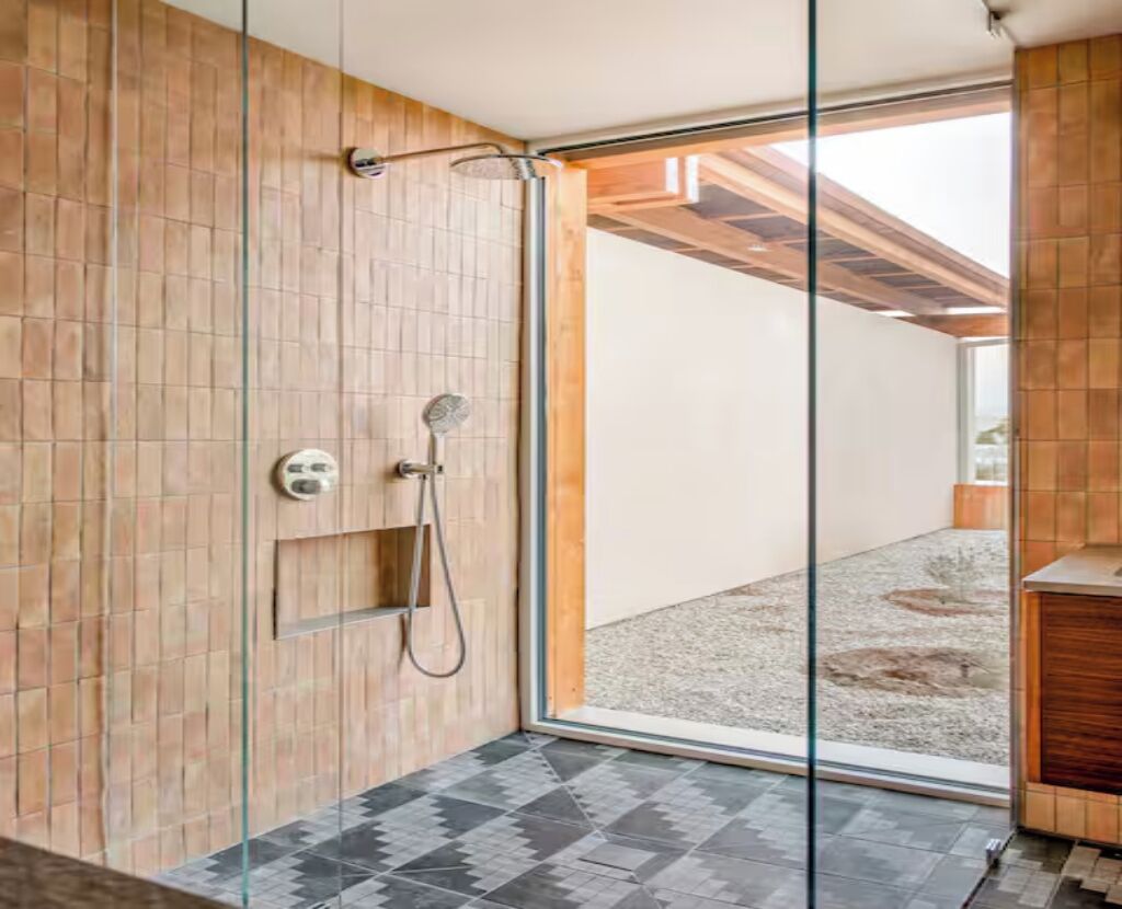 Ein modernes Badezimmer mit Duschkabine aus Glas, Holzwänden und einem sichtbaren Außenbereich mit Kies.