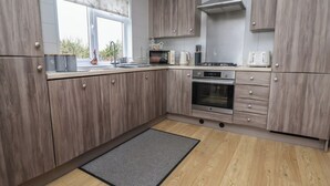 A modern kitchen with wooden cabinets, a built-in oven, and a window with a view of greenery. - Pine Lodge (Holywell)