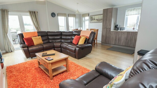 A living room with a sectional sofa, a coffee table, and a kitchen in the background. - Pine Lodge (Holywell)