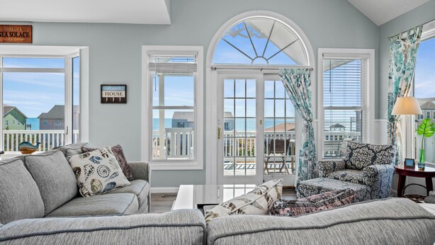 A living room with a view of the sea, a sofa, a chair, and a table with a lamp. - Spring Discount! 300ft to Beach+Heated Pool/Multiple Decks with Ocean Views (Emerald Isle)