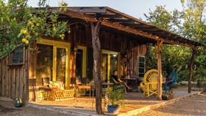 A rustic wooden building with a covered porch, outdoor seating, and a potted plant. - Aravaipa Treehouse | Farm Stay AZ (Dudleyville)
