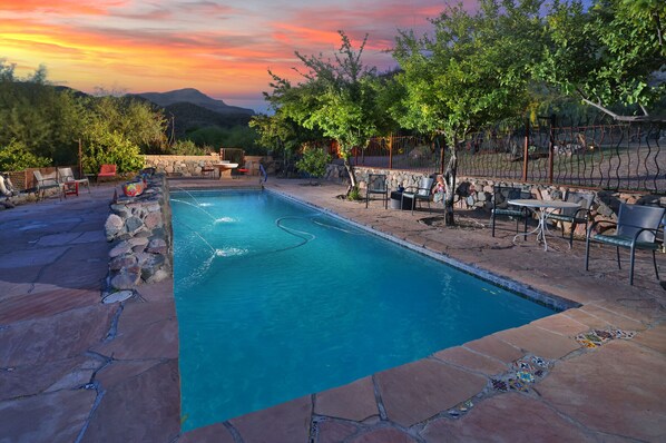 A rectangular swimming pool with a stone border, surrounded by outdoor seating and a stone wall.