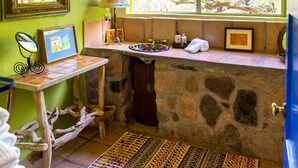 Un baño rústico con un lavabo de piedra, un espejo, una lámpara y una ventana con vistas a árboles.