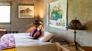 Una camera da letto con un letto, cuscini, una lampada, un comodino in legno e due quadri appesi al muro.