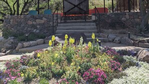 Un padiglione coperto con un muro in pietra e gradini che conducono ad esso, circondato da fiori colorati con montagne sullo sfondo.