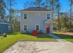 A two-story house with a red front door, a small porch, and a red Adirondack chair in the front yard.