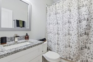 A bathroom with a white sink, a mirror, a toilet, and a shower curtain with a forest pattern.