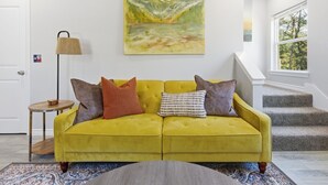Un canapé jaune agrémenté de plusieurs coussins, une lampe, un tableau et un escalier.