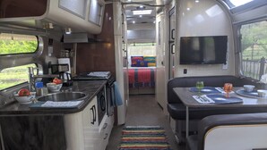 A compact RV interior with a kitchenette, a dining area, and a sleeping berth.