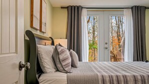 A bedroom with a bed, pillows, a bedside table, and a view of the outdoors through a door. - Sebago Pines Hideaway-Fire Pit/Beach Access/Family Friendly (Naples)
