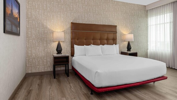 Habitación de hotel con una cama grande, dos mesitas de noche con lámparas, un papel tapiz estampado y un cuadro enmarcado en la pared.