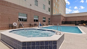 A hotel with two outdoor swimming pools, a brick facade, and a modern building in the background.