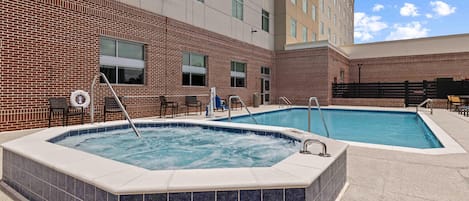 A hotel with two outdoor swimming pools, a brick facade, and a modern building in the background.