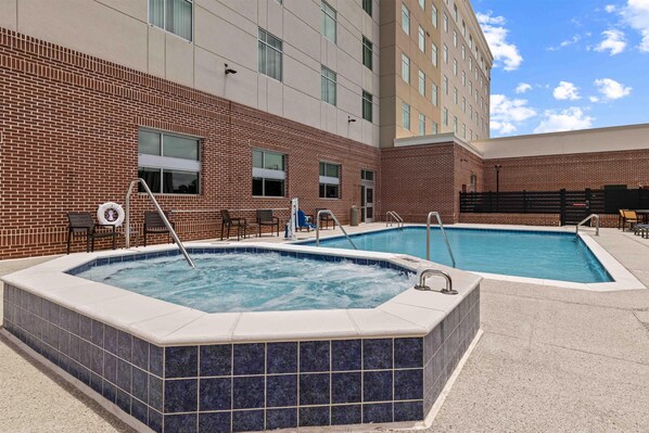 A hotel with two outdoor swimming pools, a brick facade, and a modern building in the background. - Drury Plaza Hotel Mobile (Mobile)