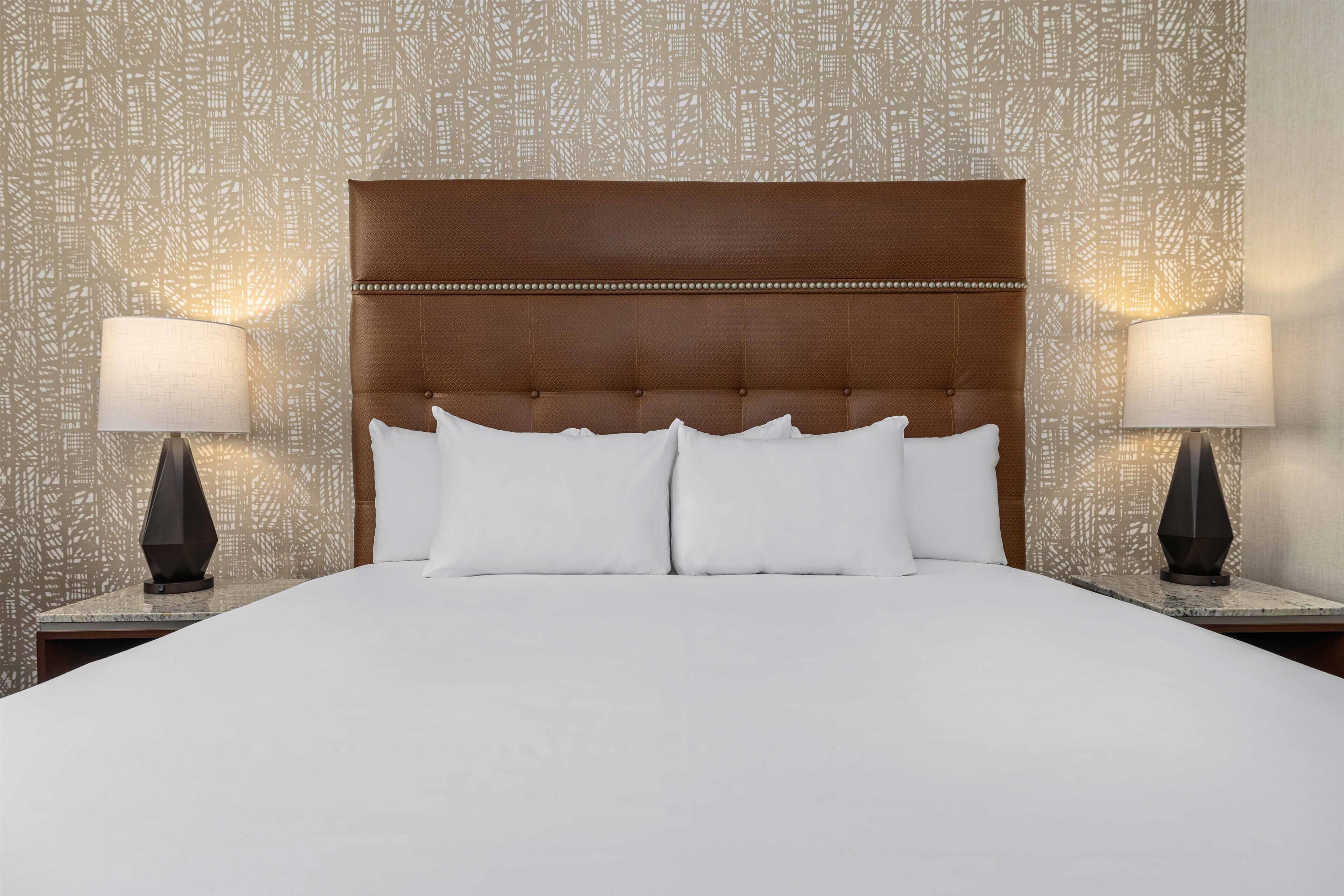 A hotel room with a large bed, two bedside lamps, and a patterned wall.